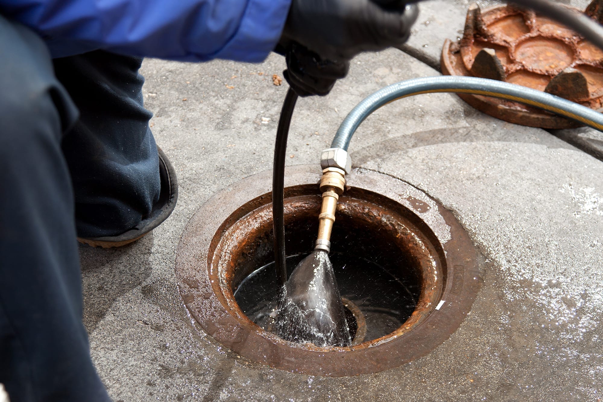 Plumber hydro jetting a sewer line through a manhole in Holladay