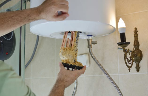 Technician removing mineral buildup from a water heater in Holladay